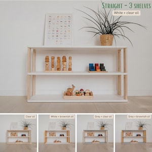 May include: A white wooden shelf unit with three shelves and natural wood supports. The unit is filled with wooden toys and decorative items. The top of the unit has a potted plant. Text on the image reads "STRAIGHT - 3 SHELVES White + clear oil".