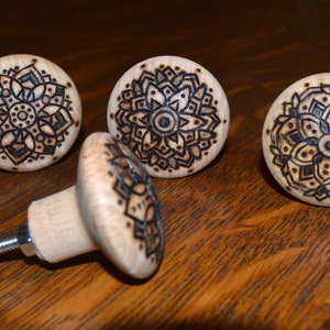 May include: Four wooden knobs with intricate mandala designs burned into the surface. The knobs are light brown with dark brown designs. One knob is attached to a metal screw.