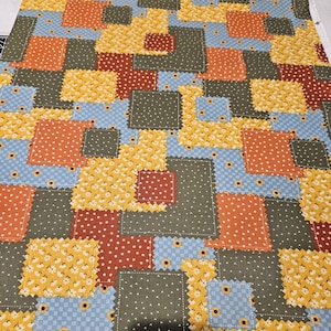 Puede incluir: Una tela de patchwork con una variedad de cuadrados coloridos. Los cuadrados presentan patrones de girasoles, lunares y pequeños diseños florales en tonos de naranja, amarillo, rojo, azul y verde. La tela tiene una apariencia texturizada.