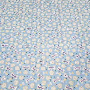 May include: Light blue fabric with a repeating pattern of dog bones, dog biscuits, and colorful sprinkles. The words "Bark Day" are printed in purple on the bones. This fabric is suitable for pet-themed crafts and projects.