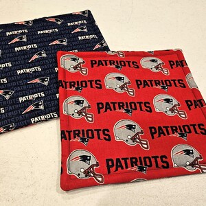 Puede incluir: Dos artículos cuadrados de tela, uno azul marino con un patrón repetido de la palabra "PATRIOTS" y logotipos del equipo, y el otro rojo con la palabra "PATRIOTS" y gráficos de casco. Estos artículos son probablemente accesorios de cocina.