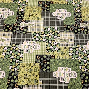 Op de afbeelding: Een patchwork stofontwerp met vierkanten met St. Patrick's Day thema's. De vierkanten bevatten ruitpatronen, klavers, hoefijzers en de zinnen "Happy St. Patrick's Day" en "Lucky" in wit en groen.