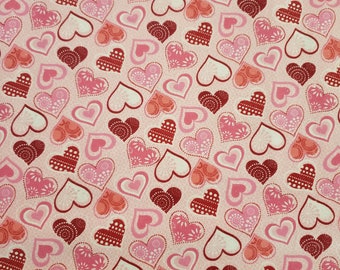 May include: A fabric with a repeating pattern of hearts in shades of pink and red. The hearts have various designs, including floral and dotted patterns, set against a light pink background.