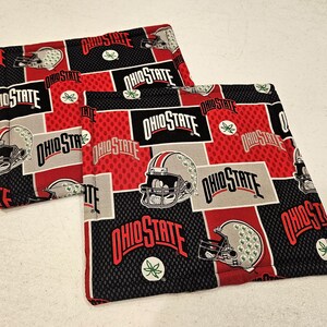 May include: Two red, black, and gray fabric pot holders with the words "Ohio State" repeated on them. The pot holders feature a football helmet design.