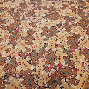 May include: A fabric with a repeating pattern of gingerbread men. The gingerbread men are in shades of brown and tan, with white icing details, red buttons, and teal accents. The overall design has a festive, holiday theme.