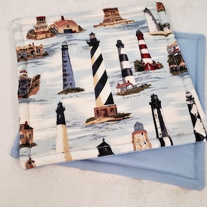 May include: A white cotton fabric coaster with a blue background featuring a variety of lighthouses with their names and locations printed on the fabric. The coaster is layered on top of a light blue fabric.