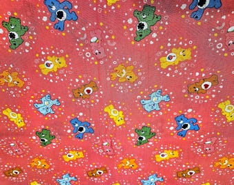 ピンクの背景にケアベア柄の生地が入ったこの商品は、1ヤード単位で販売されており、綿100％です。