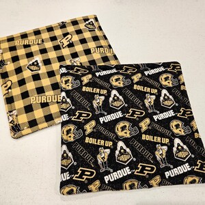May include: Two square fabric items with Purdue University designs. One features a black and gold plaid pattern with "PURDUE" text. The other has a black background with gold helmets, the letter "P", and the words "PURDUE" and "BOILER UP".