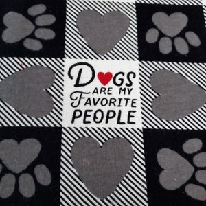 Op de afbeelding: Zwart-wit geruit stof met een grijs pootprint- en hartontwerp. De stof heeft de tekst "Dogs are my favorite people" met een rood hart in het woord "Dogs".