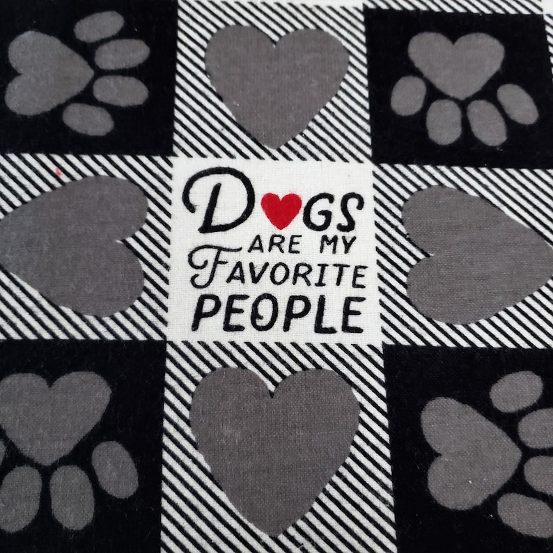 Op de afbeelding: Zwart-wit geruit stof met een grijs pootprint- en hartontwerp. De stof heeft de tekst "Dogs are my favorite people" met een rood hart in het woord "Dogs".