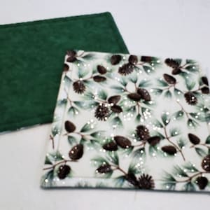 May include: Two fabric coasters, one green and one white with a pine cone pattern. The white coaster has a glittery finish.