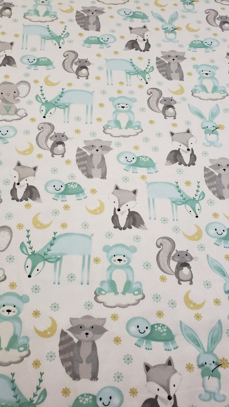 May include: A white fabric with a repeating pattern of woodland animals in shades of gray, blue, and yellow. The animals include deer, foxes, raccoons, squirrels, bears, turtles, and bunnies. The background is white with small yellow flowers.