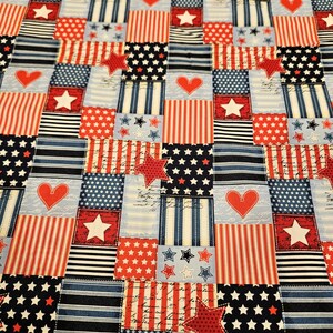 May include: A patchwork fabric with a patriotic design in red, white, and blue. The squares feature stars, stripes, hearts, and star-shaped accents. The fabric has a light blue background and a variety of patterns.