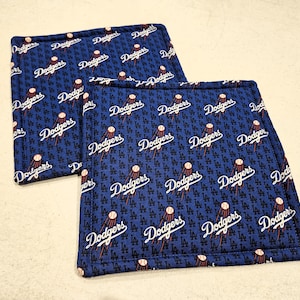 May include: Two blue fabric pot holders with a white repeated pattern of the Los Angeles Dodgers logo and baseballs.