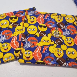 May include: Two blue fabric pot holders with a pattern of yellow smiley faces, footballs, and the words "Gator" and "1st" in red and orange.