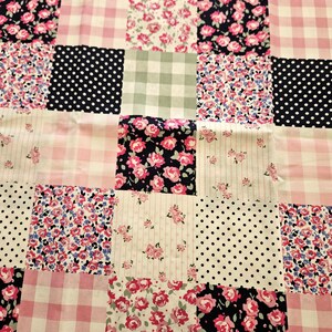 May include: A patchwork quilt featuring a variety of fabric patterns. The quilt incorporates squares of pink gingham, floral prints with pink and blue flowers, white polka dots on black, and striped patterns with pink roses.