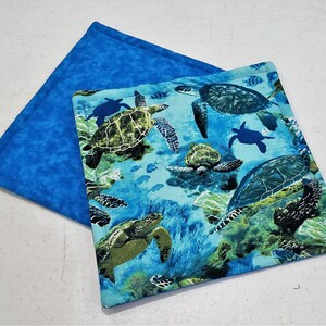 May include: Blue and green fabric pot holder with a sea turtle design. The pot holder is quilted and has a blue backing.