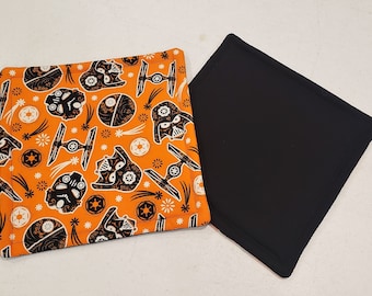 Könnte beinhalten: Ein Set aus zwei orangefarbenen und schwarzen Stoffuntersetzern. Ein Untersetzer zeigt ein sich wiederholendes Muster von Darth Vader und Star Wars X-Wing-Jäger-Silhouetten. Der andere Untersetzer ist einfarbig schwarz.