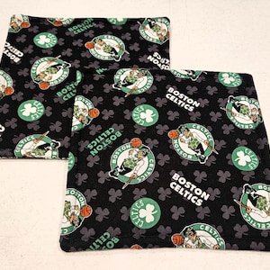 May include: Two black and green fabric pot holders with a repeating pattern of shamrocks and the Boston Celtics logo. The logo features a basketball player dribbling a basketball.