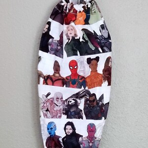 Puede incluir: Una bolsa de tela blanca con un cordón de ajuste negro y un estampado colorido de varios personajes de Marvel, incluyendo Spider-Man, Capitán América, Viuda Negra y Iron Man.