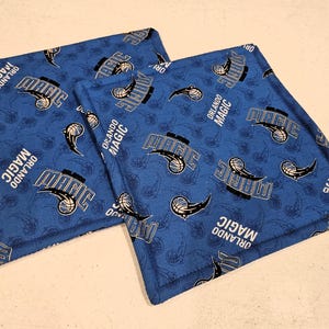 Puede incluir: Dos posavasos de tela azul con un patrón blanco y negro de balones de baloncesto y las palabras "Orlando Magic".