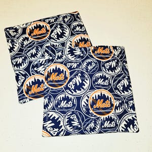 May include: Two square fabric items with a navy blue background and a repeating pattern of white baseballs and the word "Mets" in orange and white. The "Mets" logo features a cityscape.