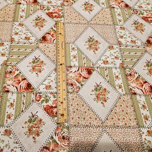 May include: A patchwork fabric with a floral pattern featuring roses in shades of peach, cream, and green. The design includes diamond and rectangular shapes, with a wooden ruler measuring in inches. The fabric is suitable for quilting and crafting projects.