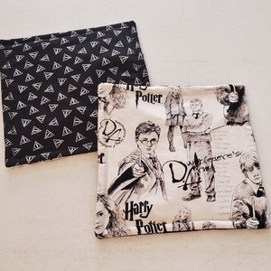 Peut inclure: Deux dessous-de-verre en tissu représentant des personnages d'Harry Potter et le symbole des Reliques de la Mort. Le premier dessous-de-verre est noir avec des triangles blancs. Le deuxième dessous-de-verre est blanc avec des illustrations noires de personnages d'Harry Potter et le texte "Harry Potter" et "L'Armée de Dumbledore".