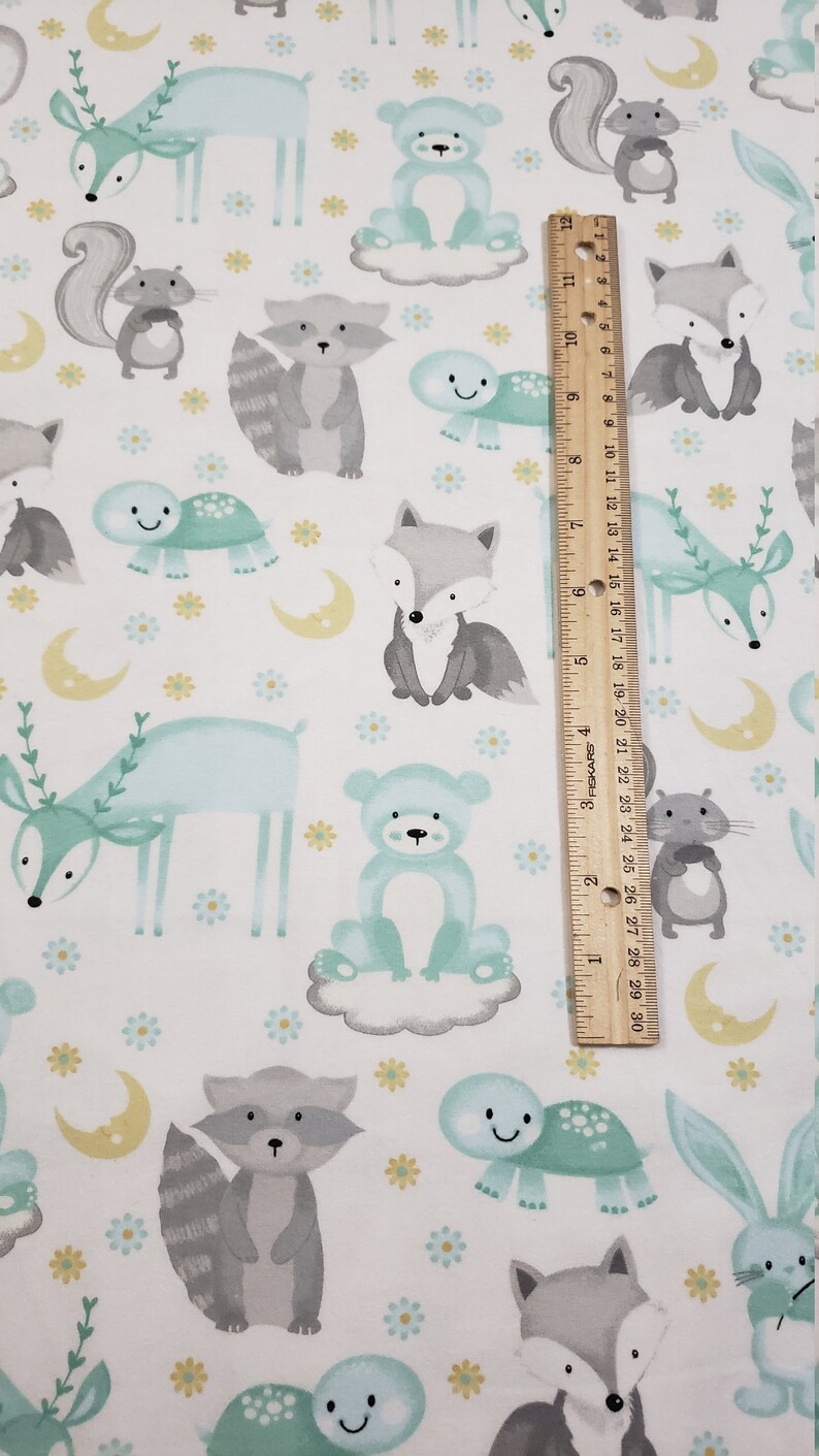May include: White fabric with a repeating pattern of woodland animals in shades of gray, blue, and yellow. The animals include a deer, fox, raccoon, bear, squirrel, and turtle. There are also small yellow flowers and crescent moons.