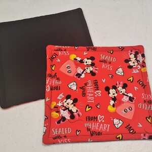 Op de afbeelding: Een rode en witte stoffen onderzetter met een Mickey Mouse en Minnie Mouse ontwerp. De stof heeft een herhalend patroon van harten, enveloppen en de tekst "From my heart to yours" en "Sealed with a kiss".