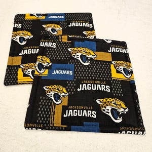 Könnte beinhalten: Schwarze Stoffuntersetzer mit dem Logo und dem Teamnamen der Jacksonville Jaguars in Weiß und Gold. Die Untersetzer haben ein sich wiederholendes Muster des Jaguar-Kopf-Logos des Teams und das Wort "Jaguars".