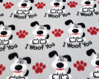 Puede incluir: Tela de franela gris con un patrón repetido de perros de dibujos animados blancos con orejas y narices negras. Los perros llevan collares rojos y el texto "I Woof You" está impreso debajo de cada perro. Las huellas de patas rojas están dispersas por toda la tela.