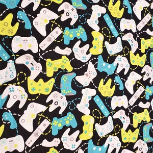 May include: A black fabric with a repeating pattern of colorful video game controllers. The controllers are in shades of white, yellow, blue, and green. The background is black with a dashed line pattern.