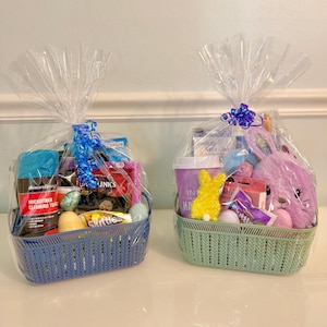 May include: Two Easter baskets, one blue and one green, filled with treats and wrapped in cellophane. The blue basket contains cleaning supplies, candy, and Easter eggs. The green basket has a plush bunny, candy, and a yellow bunny decoration.