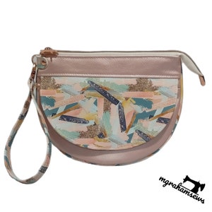 May include: A half-moon shaped zippered pouch with a pink and white fabric exterior. The pouch has a colourful abstract print with gold glitter accents. The pouch has a short handle.