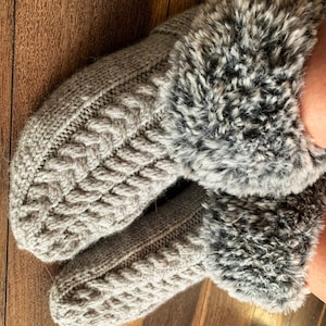 May include: A pair of gray knitted slippers with a faux fur cuff. The slippers have a cable knit pattern and are soft and cozy.