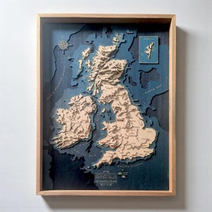 May include: A three-dimensional wooden bathymetric map of the British Isles framed in light wood. The landmasses are light tan, while the deep ocean areas are dark blue. The map features engraved text, a compass rose, and a small inset map.