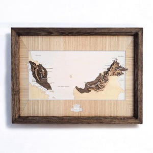 Può includere: Mappa in legno incorniciata della Malesia con un design tridimensionale dettagliato. La mappa presenta uno sfondo chiaro con ritagli in legno marrone scuro e beige che rappresentano la massa terrestre e la topografia del paese. La cornice è marrone scuro.