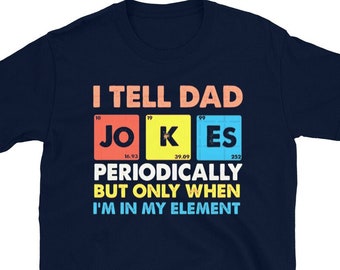 Puede incluir: Una camiseta azul marino de manga corta con el texto I TELL DAD JOKES PERIODICALLY BUT ONLY WHEN I'M IN MY ELEMENT. La palabra JOKES está diseñada como elementos de la tabla periódica en cuadrados rojos, amarillos y azules con números.