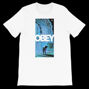K&ouml;nnte beinhalten: Wei&szlig;es T-Shirt mit einem blauen und wei&szlig;en Grafikdruck eines Mannes, der sich vor einer Wand mit einem blauen und wei&szlig;en Muster verbeugt. Die Grafik enth&auml;lt auch das Wort "OBEY" in wei&szlig;en Buchstaben.