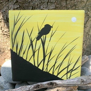 May include: A black silhouette of a bird perched on a tall stalk of grass against a yellow background with a white moon in the top right corner.