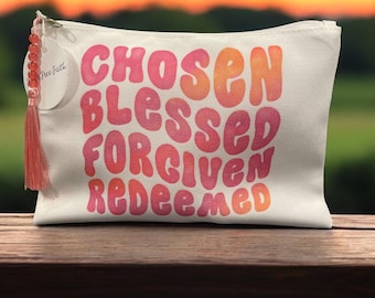 May include: A white canvas zippered pouch with the words "Chosen Blessed Forgiven Redeemed" in pink and orange lettering. The pouch has a pink tassel attached to it.