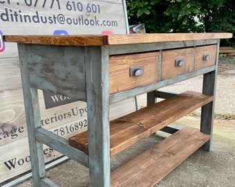 May include: A rustic wooden console table with three drawers and two shelves. The table is painted in a light blue color with a distressed finish. The drawers have metal handles and the shelves are made of unfinished wood.