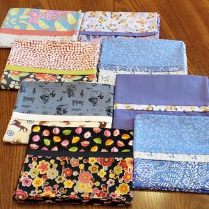 May include: A stack of colorful pillowcases with various patterns, including floral, butterfly, and geometric designs. The pillowcases are in shades of blue, pink, and black, and are neatly folded and stacked on a wooden surface.