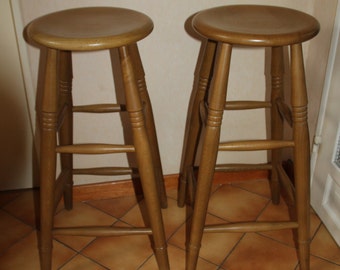 May include: Two wooden bar stools with a brown finish. The stools have a simple design with a round seat and four legs.