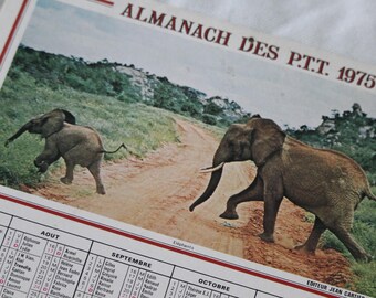 Op de afbeelding: Vintage kalender uit 1975 met een kleurenfoto van twee olifanten op een zandweg. De kalender heeft de tekst "ALMANACH DES P.T.T. 1975" en bevat maandelijkse datumroosters. Een nostalgisch stuk.