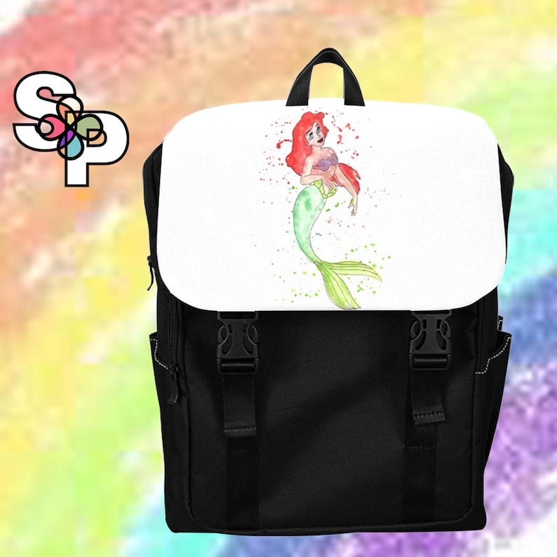 K&ouml;nnte beinhalten: Ein schwarzer Rucksack mit einer wei&szlig;en Klappe, die eine Aquarellillustration einer Meerjungfrau mit rotem Haar und gr&uuml;nem Schwanz zeigt. Der Rucksack hat zwei schwarze Schnallenriemen auf der Vorderseite und ein Logo mit den Buchstaben SP oben links.