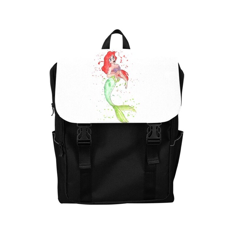 K&ouml;nnte beinhalten: Ein schwarzer Rucksack mit einer wei&szlig;en Klappe, die eine Aquarellillustration einer Meerjungfrau mit langem rotem Haar und gr&uuml;nem Schwanz zeigt. Der Rucksack verf&uuml;gt &uuml;ber zwei schwarze vertikale Riemen mit Kunststoffschnallen und einen Tragegriff.