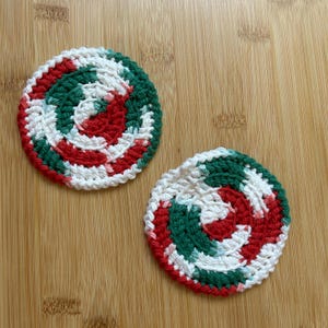 May include: Two crocheted coasters in a red, white, and green spiral pattern. The coasters are round and have a white background with red and green stripes.