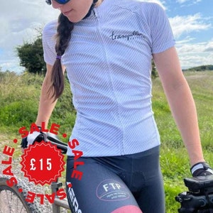 May include: A white cycling jersey with a black and white striped pattern. The jersey has a black zip and the text "tranquilla cycling" on the back. The jersey is on sale for £15.